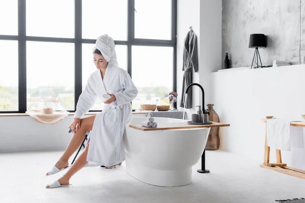 Mujer aplicando crema cosmética en la pierna en el baño - foto de stock