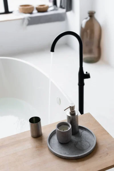 Candle and toiletries on bathtub tray near faucet on blurred background — Stock Photo