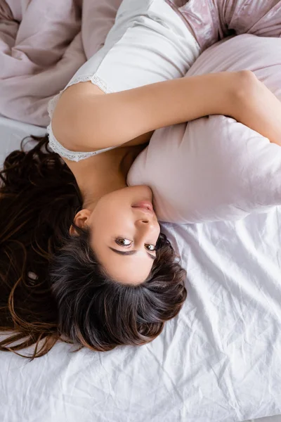 Top view of woman looking at camera while hugging pillow on bed — Stock Photo