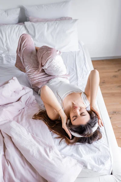 Vista de alto ângulo da mulher no pijama e fones de ouvido deitados na cama durante a manhã — Fotografia de Stock