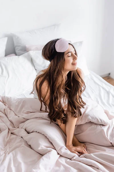 Brunette woman in blindfold sitting on bed at home — Stock Photo