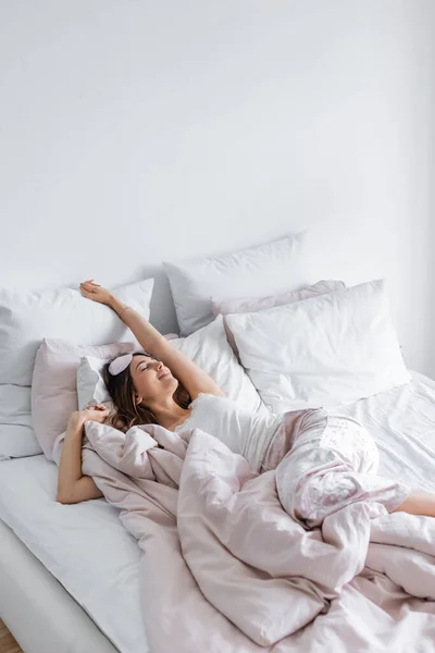 Pleased woman in pajama and blindfold lying with closed eyes on bed — Stock Photo
