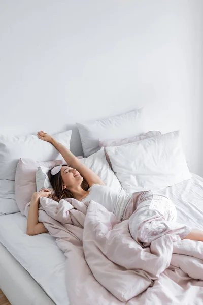 Mujer agradable en pijama y ojos vendados acostada con los ojos cerrados en la cama - foto de stock