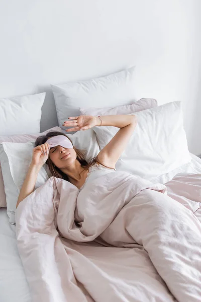 Brunette woman holding blindfold on bed at home — Stock Photo