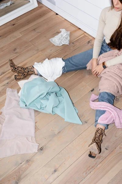 Cropped view of clothes on floor near woman sitting in wardrobe — Stock Photo