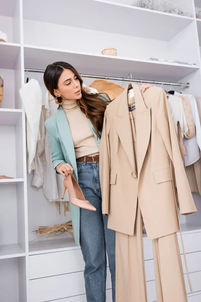 Stilvolle Frau hält Anzug auf Kleiderbügel und Schuh im Kleiderschrank — Stockfoto