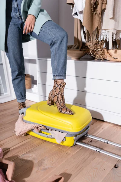 Обрезанный вид женщины положить ноги на чемодан с одеждой в шкафу — стоковое фото