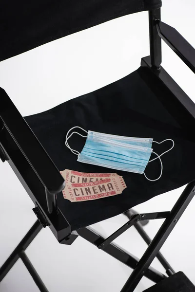 Vue grand angle des masques médicaux et billets de cinéma sur chaise de cinéaste sur blanc, concept de cinéma — Photo de stock