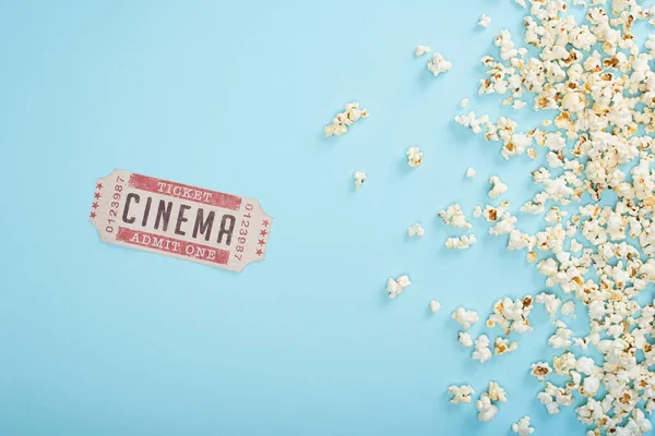 Top view of cinema ticket near scattered popcorn on blue — Stock Photo