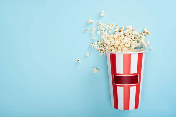 Top view of striped carton bucket with popcorn on blue, cinema concept — Stock Photo