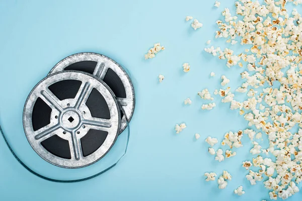 Ansicht von Filmrollen in der Nähe von verstreutem Popcorn auf blauem Grund, Kinokonzept — Stockfoto