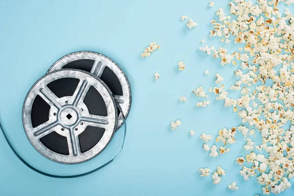 Vista superior de carretes de película cerca de palomitas de maíz dispersas en azul, concepto de cine — Stock Photo