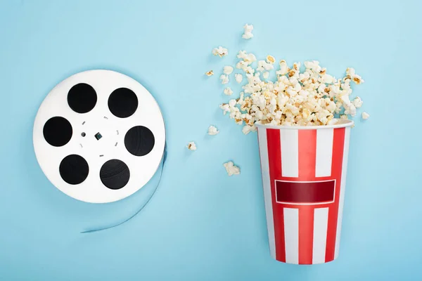 Vista dall'alto della bobina di film vicino secchio di popcorn su blu, concetto di cinema — Foto stock