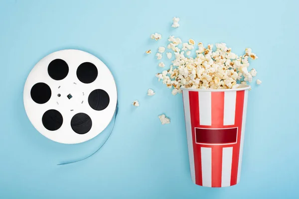 Vue du dessus de la bobine de film près du seau de maïs soufflé sur bleu, concept de cinéma — Photo de stock