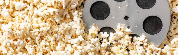 Top view of film bobbin on airy delicious popcorn, banner, cinema concept — Stock Photo