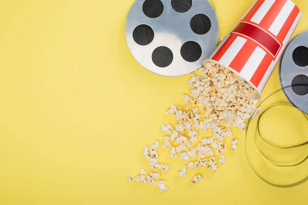Top view of film reels near bucket with scattered popcorn on yellow, cinema concept — Stock Photo