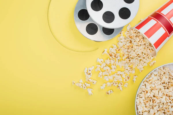 Top view of film coils near buckets with popcorn on yellow, cinema concept — Stock Photo