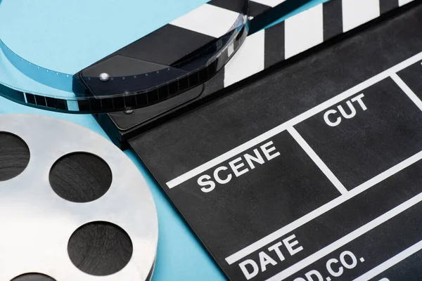 Vue rapprochée du clapperboard et de la bobine de film sur bleu, concept cinéma — Photo de stock