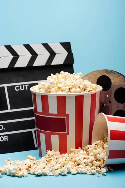 Seaux de pop-corn, clapperboard et bobine de film sur bleu, concept de cinéma — Photo de stock