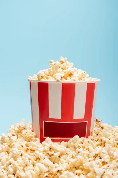 Striped bucket and pile of tasty popcorn isolated on blue, cinema concept — Stock Photo