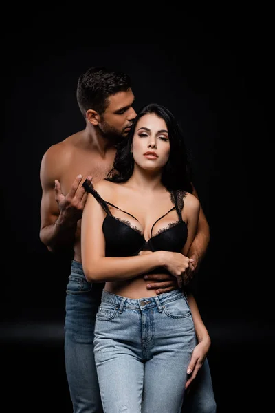 Muscular man holding strap of bra on sexy woman isolated on black — Stock Photo