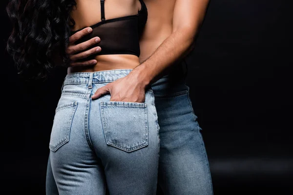 Vista ritagliata dell'uomo sexy che mette mano in tasca di jeans sulla ragazza isolata sul nero — Foto stock