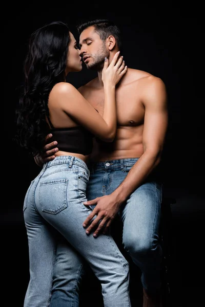 Сексуальная женщина целует бойфренда в джинсах, изолированных на черном — стоковое фото