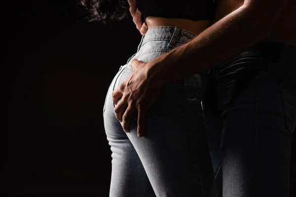 Cropped view of man touching butt of girlfriend in jeans isolated on black — Stock Photo
