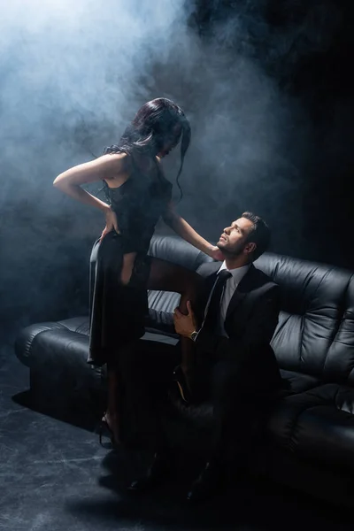 Donna sexy in abito in piedi vicino fidanzato in tuta sul divano — Foto stock