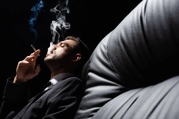Mann in offizieller Kleidung raucht Zigarette auf schwarzer Couch — Stockfoto