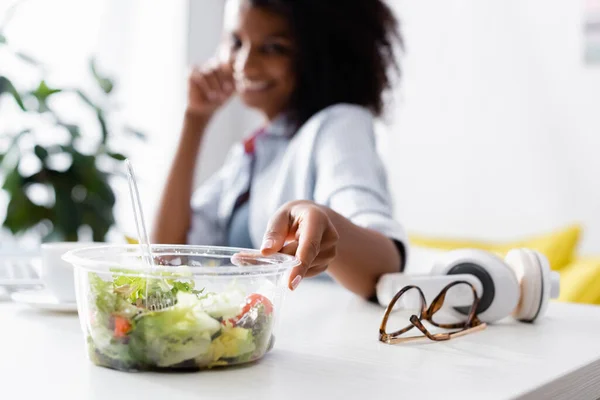 Takeaway salada perto de óculos e mulher americana africana no fundo borrado — Fotografia de Stock