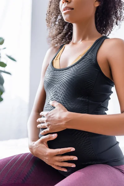 Vista cortada da grávida afro-americana esportista tocando barriga em casa — Fotografia de Stock