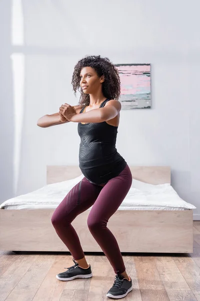 Embarazada mujer afroamericana haciendo ejercicio en el dormitorio - foto de stock