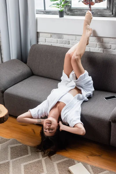 Jeune femme adulte reposant avec les jambes dans l'air sur le canapé gris à la maison — Photo de stock