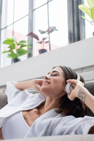 Joyful young adult woman listening music in headphones on couch at home — Stock Photo