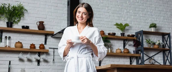 Pretty young adult woman in bathrobe drinking coffee and looking at camera in modern loft, banner — Stock Photo