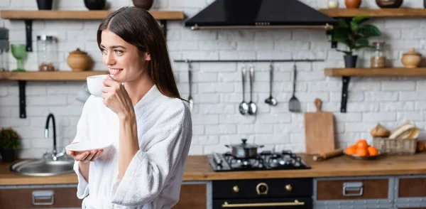 Sonriente mujer joven adulta en albornoz beber café en el loft moderno, pancarta - foto de stock