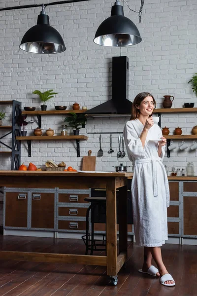 Vue pleine longueur de heureuse jeune femme adulte en peignoir boire du café dans le loft moderne — Photo de stock