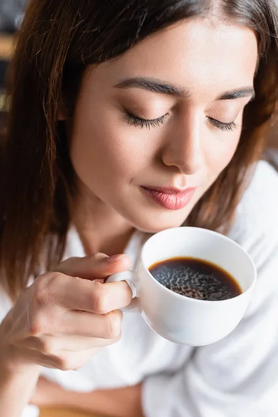 Vista de ángulo alto de la mujer joven adulta bebiendo café con los ojos cerrados sobre fondo borroso - foto de stock