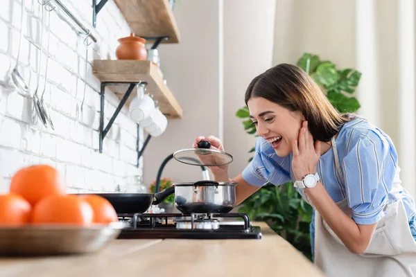 Happy young adult woman cooking near burner in modern kitchen — Stock Photo