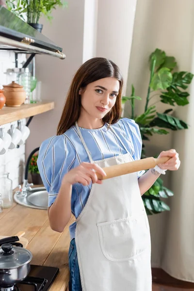 Bella giovane donna adulta in grembiule in piedi con mattarello pasta in cucina moderna — Foto stock