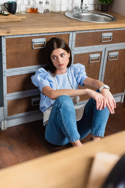 Mujer adulta joven agotada sentada en el suelo en la cocina moderna - foto de stock