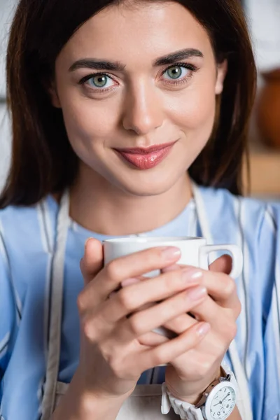 Porträt einer lächelnden jungen erwachsenen Frau mit einer Tasse Kaffee in der Hand auf verschwommenem Hintergrund — Stockfoto