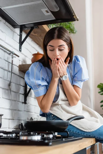 Напряженная молодая женщина закрывает рот руками возле горелки на кухне — стоковое фото