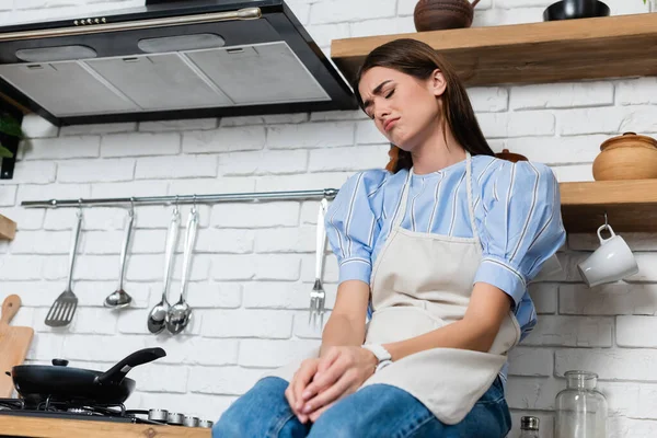 Disappointed young adult woman sitting near burner in kitchen — Stock Photo