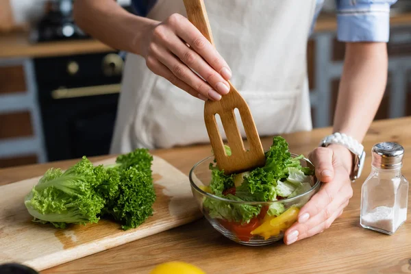Partial view of young adult woman mixing vegetables salad with spatula in kitchen — Stock Photo