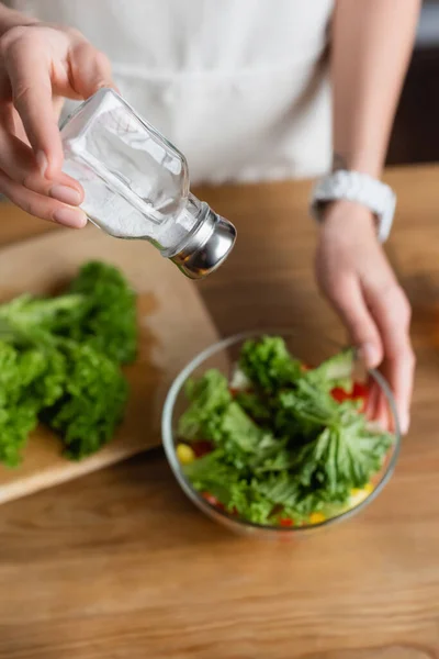 Teilansicht einer jungen erwachsenen Frau, die in der Küche frischen Gemüsesalat mit Salzmühle würzt — Stockfoto