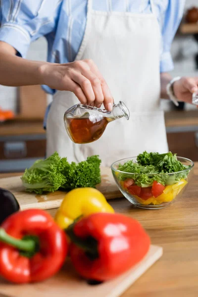 Partial view of young adult woman seasoning fresh vegetables salad with olive oil in kitchen — Stock Photo