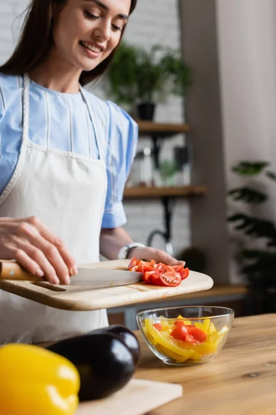 Giovane donna adulta che mette pomodori ciliegini affettati nell'insalata di verdure nella cucina moderna — Foto stock