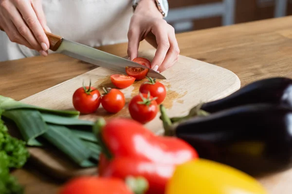 Partial view of young adult woman cutting cherry tomatoes on chopping board in modern kitchen — Stock Photo